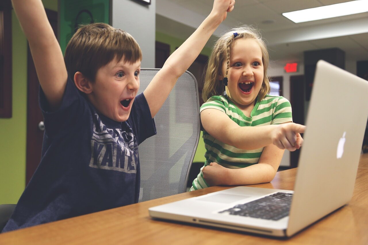 Two children excitedly saying 'Yay!' while looking at a computer screen, symbolizing the joy of finding the perfect hotel deal through Hotellook.